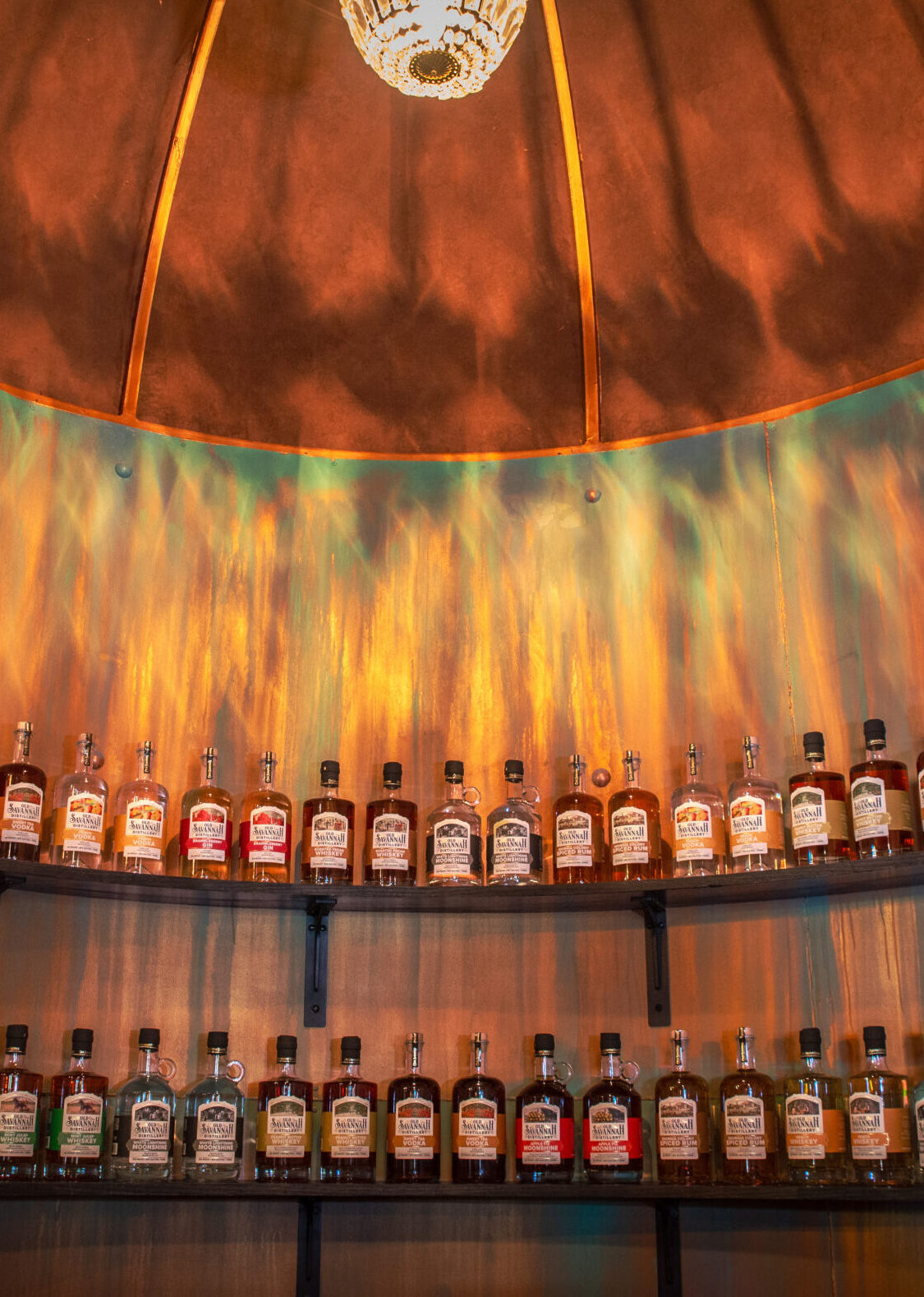 Shelves of old savannah distillery bottles under warm glowing copper wall