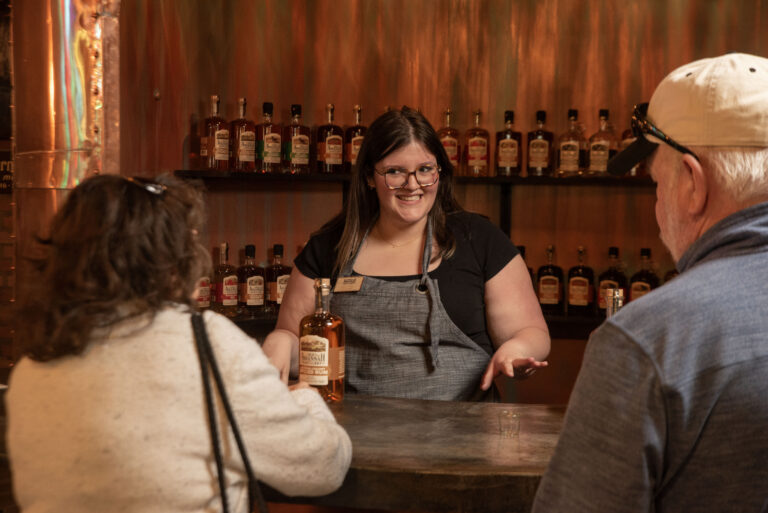 Bartender serving whiskey to two guests at a tasting bar.